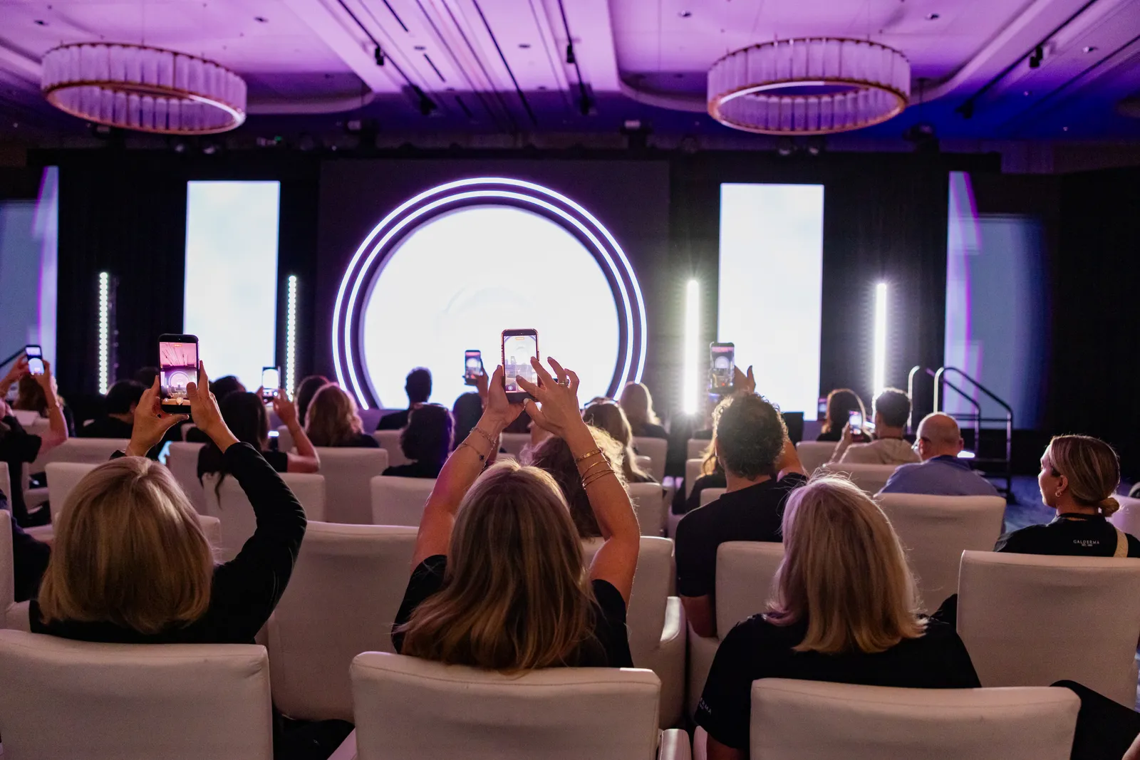 An audience photographing the main stage at a corporate program